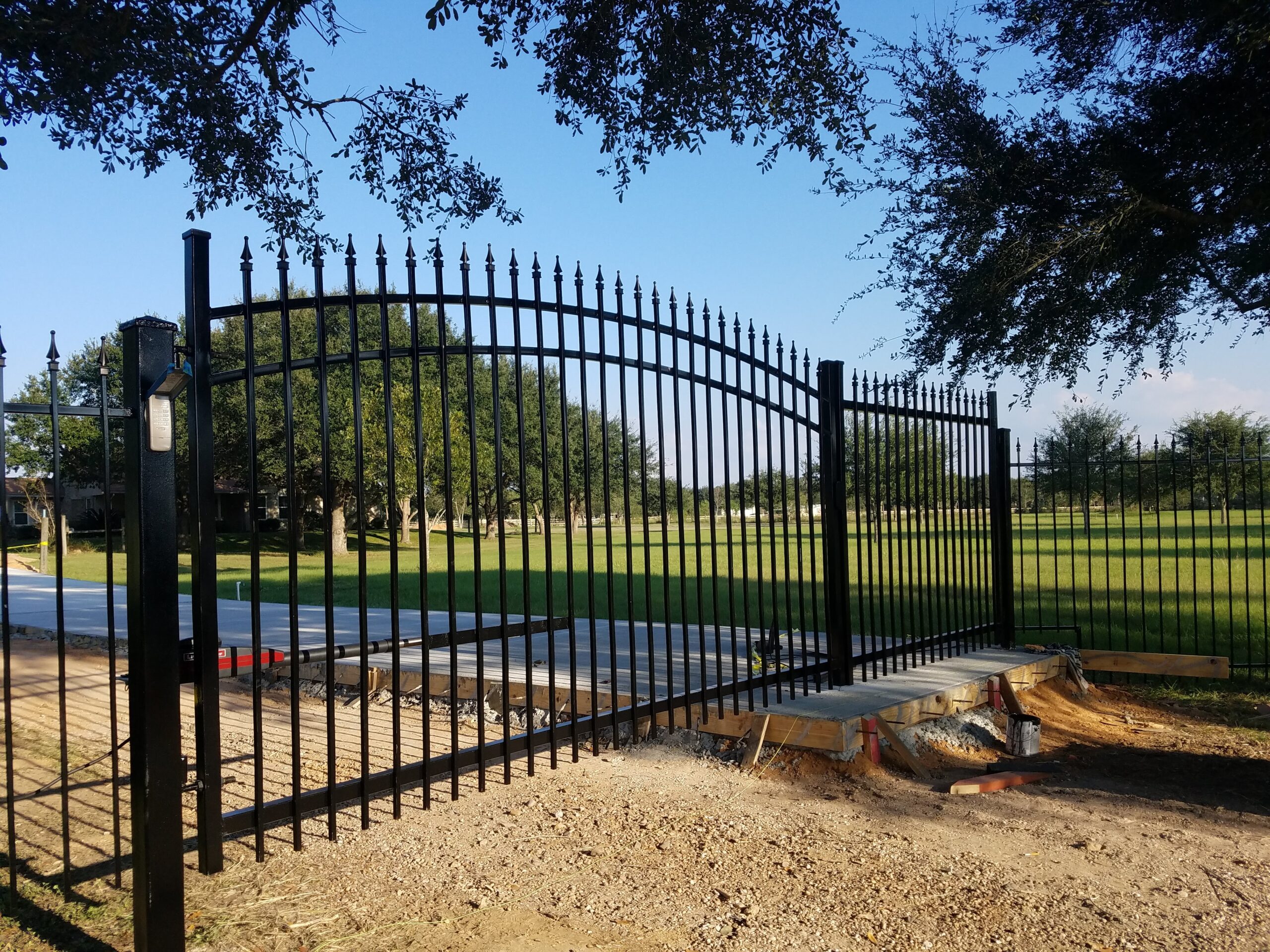 Arched black wrought iron driveway gate with matching powder coated fence for a Houston property