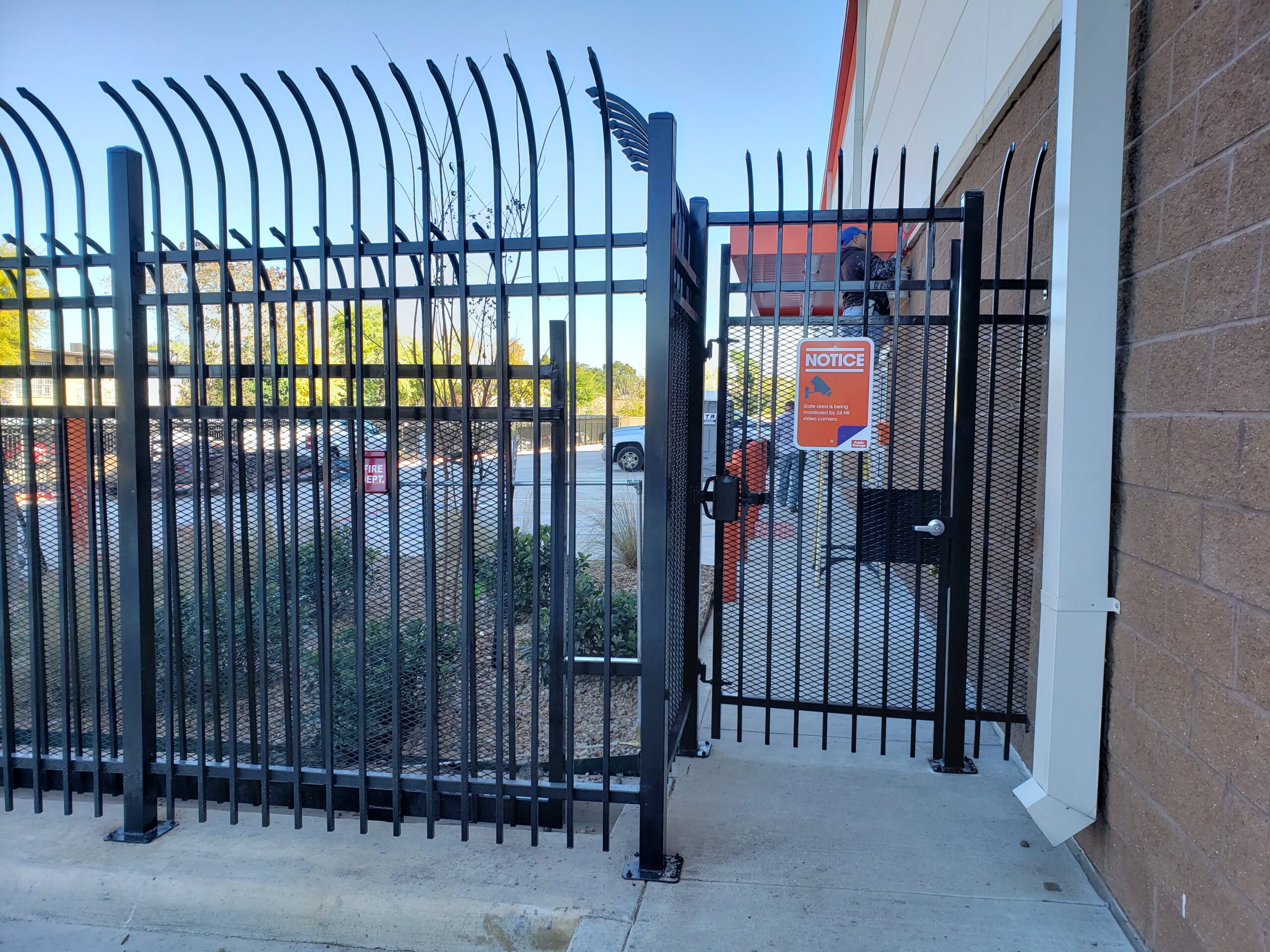 Commercial black metal security fence with pedestrian access gate beside a Houston business property