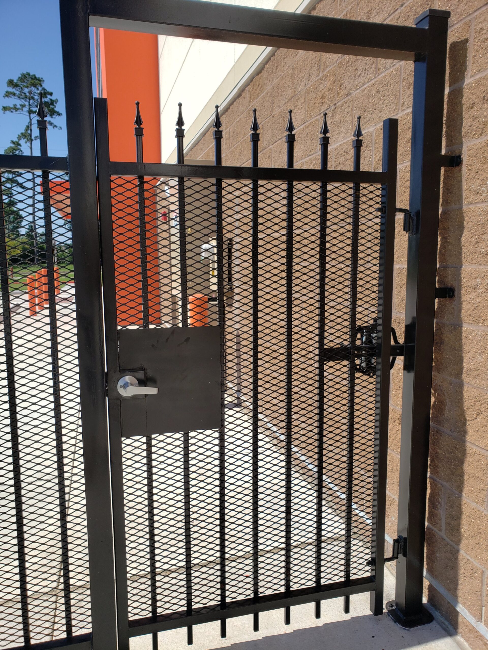 Commercial pedestrian security gate with mesh infill and lock hardware at a Houston business property